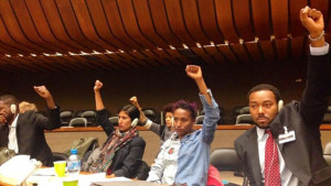 During a hearing, the Ferguson to Geneva, delegation lifts their fists in solidarity with the youth-led We Charge Genocide delegation from Chicago (not pictured). From right to left, Justin Hansford, Tara Thompson, and Meena Jagannath. Photo/Charles Wade/Ferguson to Geneva.
