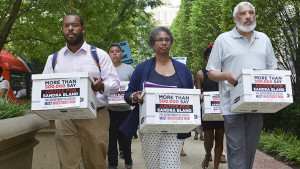(Left-Right) Eugene Puryear of the Stop Police Terror Project in Washington, D.C., Lois Wilkins, the Freeland, Mich., resident and mother of four who started the petition on MoveOn.org, and Reverend Graylan Hagler, the senior pastor of the Plymouth Congregational United Church of Christ carry boxes of signed petitions to the visitor&rsquo;s entrance of the Department of Justice. Photo/Freddie Allen/NNPA News Wire.